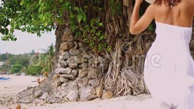 年轻的黑发女人，长发，戴着白色的树和帽子，走在热带海滩上。 慢动作。 3840x2160